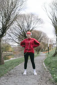 Kvinne i rødt treningsantrekk tar en pause under utendørs trening i park — illustrerer at generell trening som gåtur og løping kan hjelpe ved langvarige nakke- og skuldersmerter.